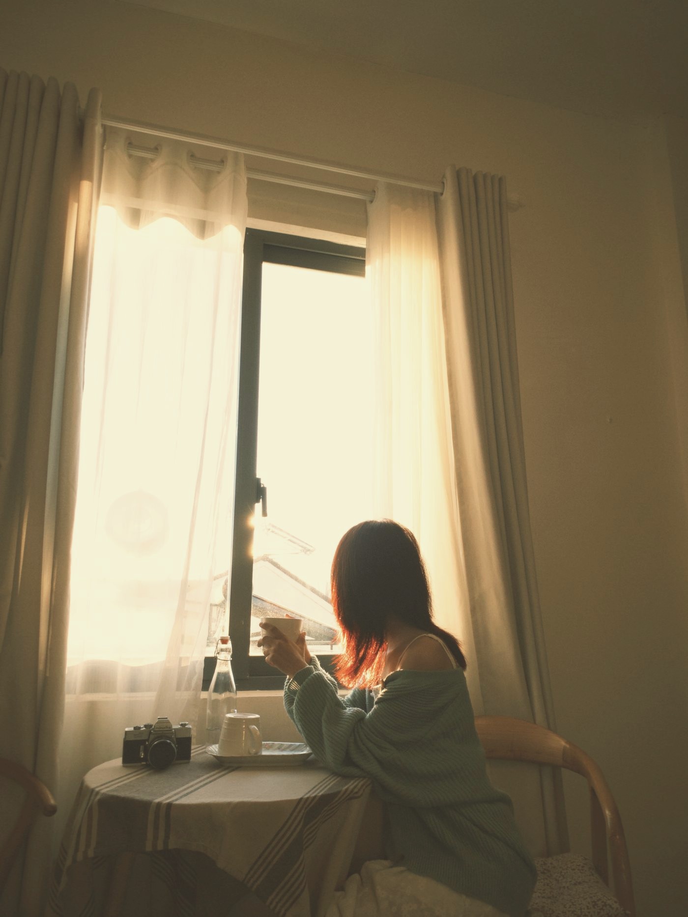 A woman with coffee in warm window light. A morning scene, not a portrait of the founder.
